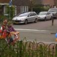 Op de fiets naar de Koningsspelen Kinderen rijden op versierde fietsen naar de Koningsspelen. Een lint van oranje, rode, witte en blauwe kleuren komt voorbij. Ze dragen hun koningsspelent-shirt. Zachtjes gaat het regenen. Het aantal kinderen...
